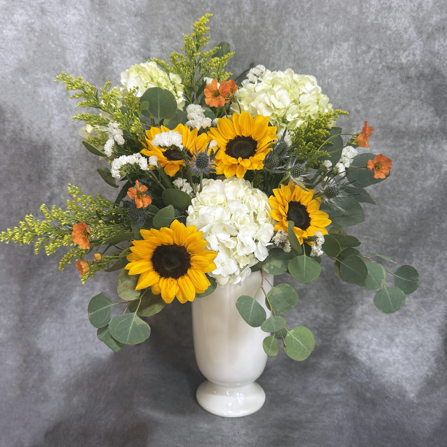 Bouquet of sunflowers and hydrangeas in a white vase on a gray background