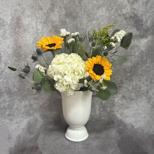 Floral arrangement with sunflowers and white flowers in a white vase on a gray background