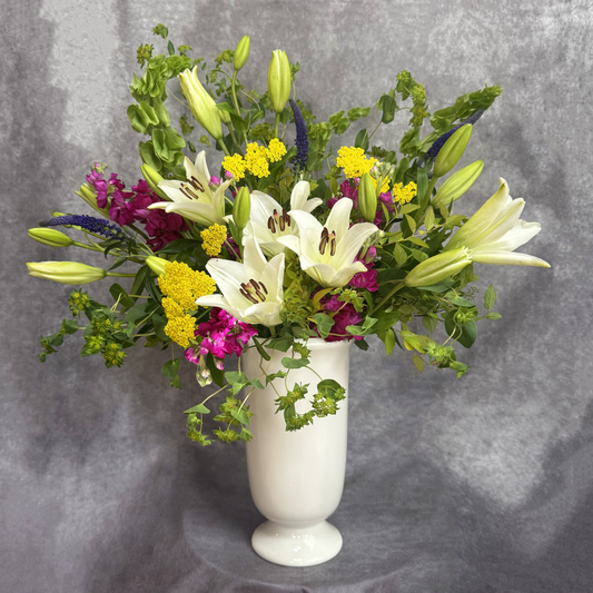 Floral arrangement with white lilies, yellow flowers, and greenery in a white vase on a gray background