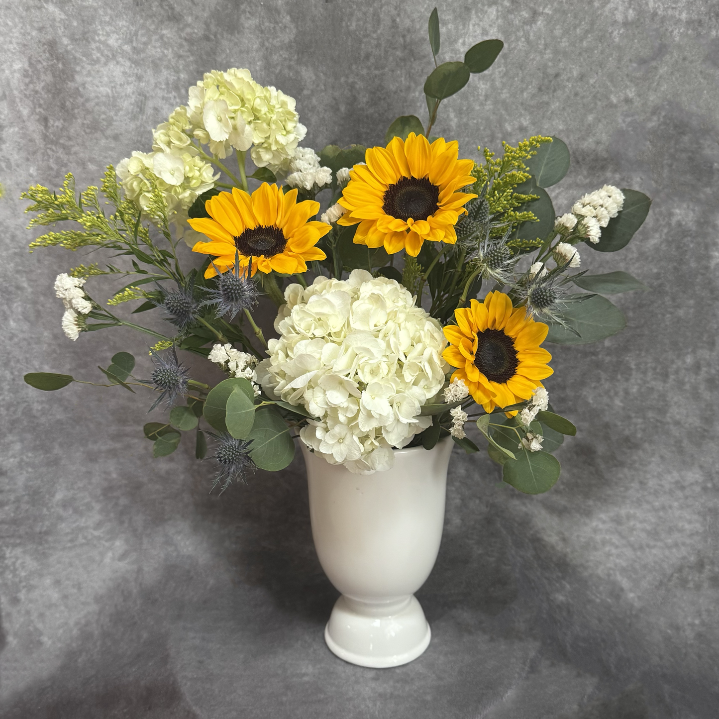 Floral arrangement with sunflowers and hydrangeas in a white vase on a gray background