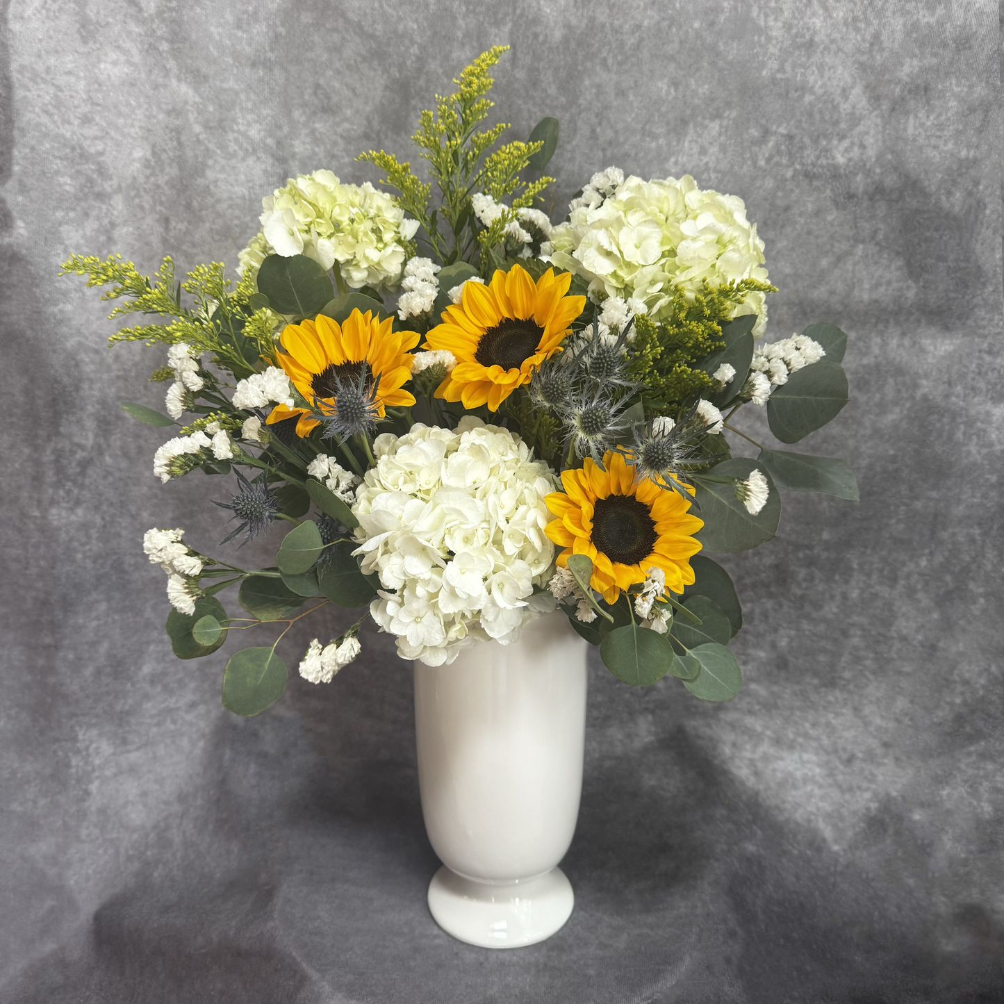 Floral arrangement with sunflowers and white flowers in a white vase on a gray background