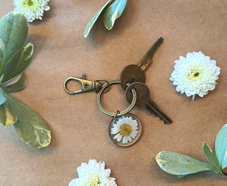 Keychain with a daisy charm on a craft paper surface with flowers and leaves.